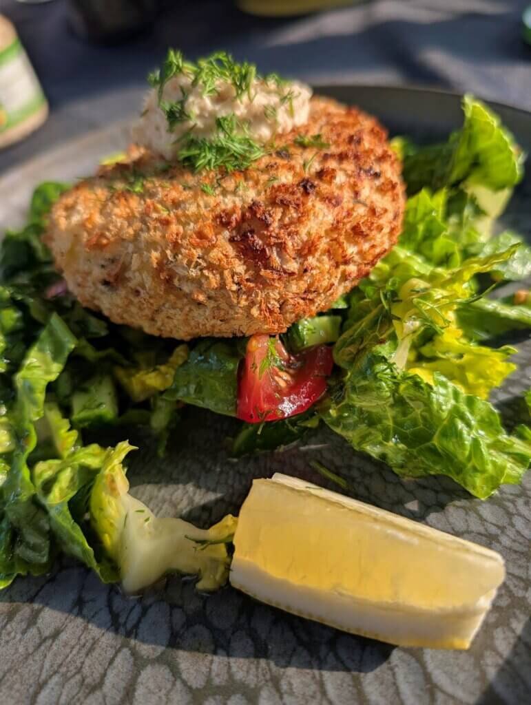 Würzige Lachs-Garnelen-Pflanzerl Cajun Style - Knusprige Fish Cakes vom Grill serviert auf einem Teller mit Salat und Dip