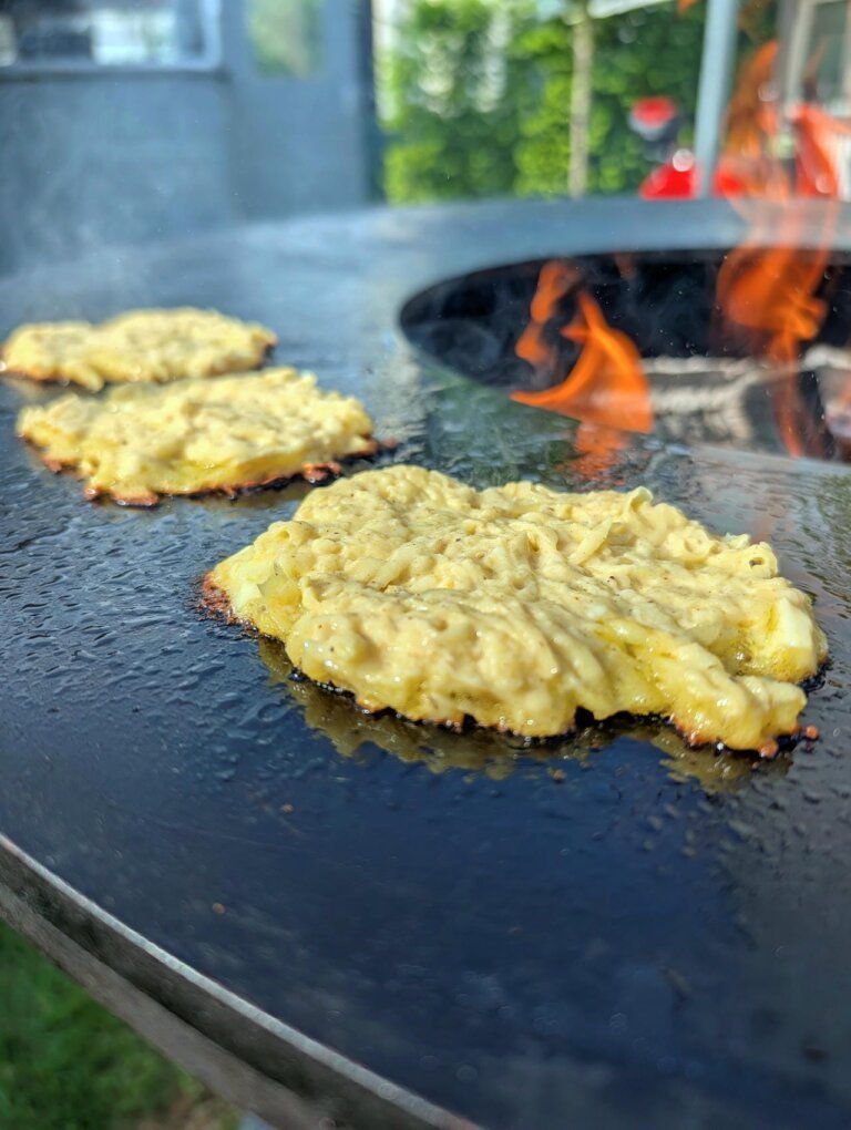 Mehrere Kartoffelru00f6sti brutzeln nebeneinander auf der eingeu00f6lten Grillplatte des Grills