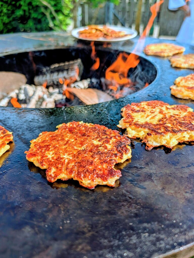 Wenden der Kartoffelru00f6sti mit einem Grillspachtel auf der heiu00dfen Gussplatte fu00fcr eine gleichmu00e4u00dfige Kruste