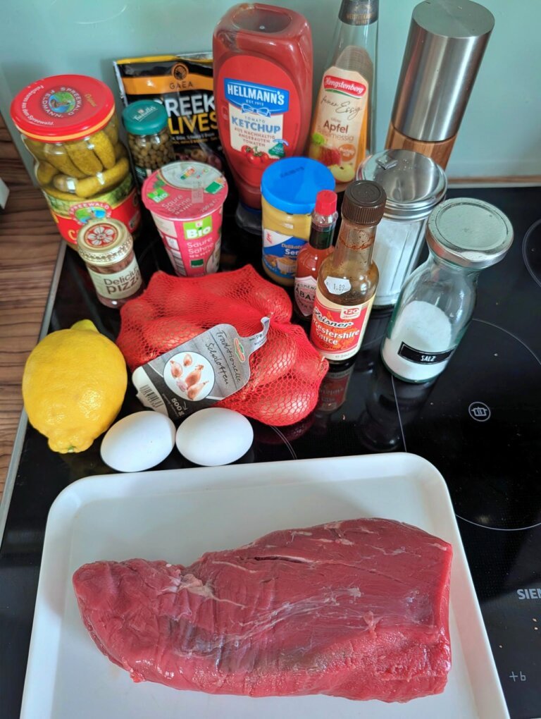 Heiß-Kaltes Steak Tatar 4 Übersicht aller benötigten Zutaten für Steak Tatar, darunter Fleisch, Eigelb, Kapern und Gewürze.